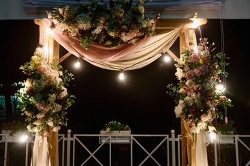 Night wedding ceremony with arch, flowers, cloth and bulb lights on the backyard outdoors, copy space. Wedding decor
