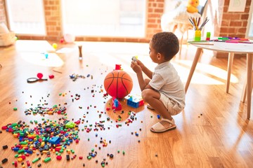 Beautiful african american toddler playing with cars around lots of toys at kindergarten