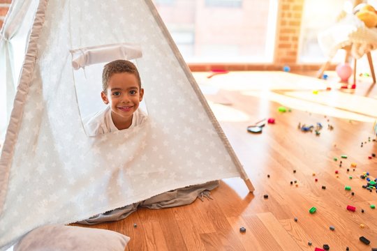 Beautiful african american toddler playing inside tipi smiling at kindergarten