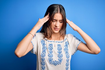 Young beautiful brunette woman wearing casual t-shirt standing over blue background with hand on head for pain in head because stress. Suffering migraine.