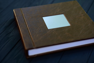 A metal nameplate on the cover of a brown leather photo book on a black wooden background.