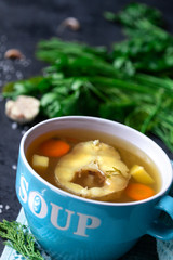 Fresh fish soup in a blue bowl on a dark background with herbs. Close-up