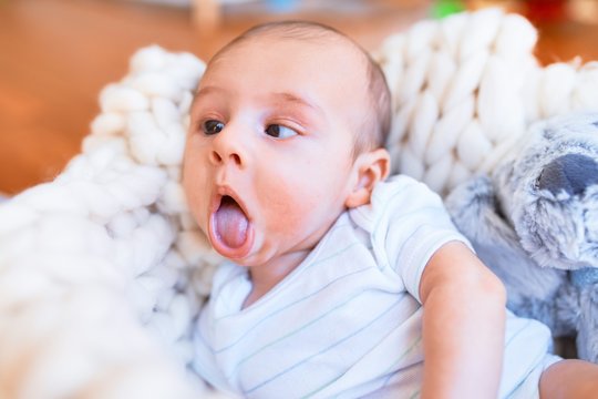 Adorable baby lying down over blanket on the floor at home. Newborn relaxing and resting comfortable with teddy bear