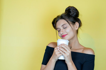 Young pretty woman with take away coffee cup. Young girl at yellow background, copy space