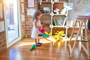 Adorable blonde toddler playing around lots of toys at kindergarten