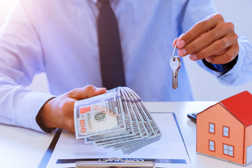 business man giving house with keys of customer and holding dollar us bank at agency office....