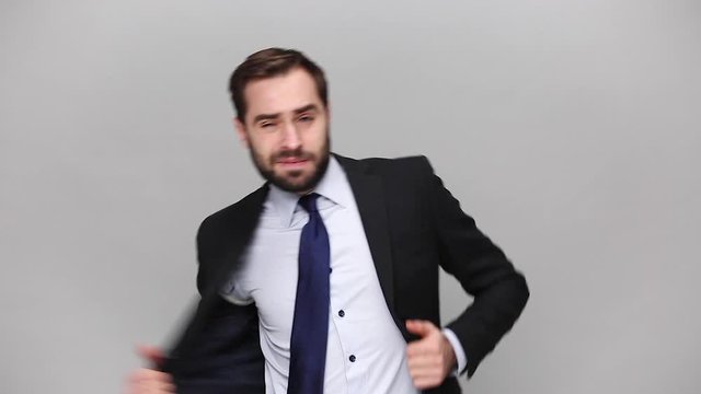 Fun bearded young business man in classic black suit shirt tie posing isolated on grey background studio. Achievement career wealth business concept. Mock up copy space. Take off jacket dance rejoice