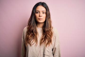Fototapeta premium Young beautiful brunette woman wearing casual sweater standing over pink background Relaxed with serious expression on face. Simple and natural looking at the camera.
