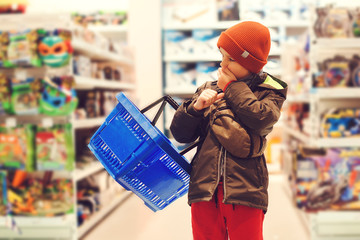 Little kid holding shopping cart in kids store. Boy choosing toy in big assortement in supermarket. It is difficult choice to buy a interesting toy
