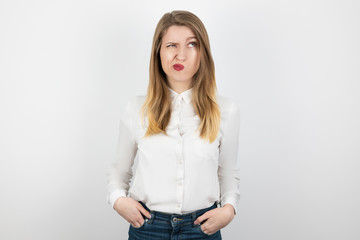 young beatuiful blond woman looks hesitant standing on isolated white background, body language