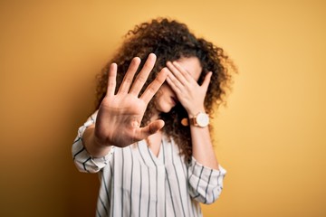Young beautiful woman with curly hair and piercing wearing striped shirt and glasses covering eyes...