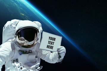 Spaceman in open space shows a card with your text here on the background of planet earth....