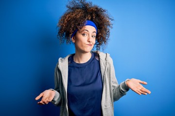 Young beautiful sportswoman with curly hair and piercing standing wearing sportswear clueless and...
