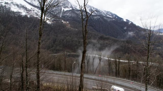 Aerial view of a car moving on curved road located in mountains. Stock footage. Flying over late autumn forest and snowy mountains.