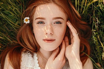 Redhead girl lying on green grass - obrazy, fototapety, plakaty