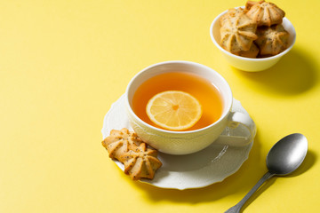 Tea with lemon in a white Cup and lemon cookies with poppy seeds in a white ceramic bowl on a...