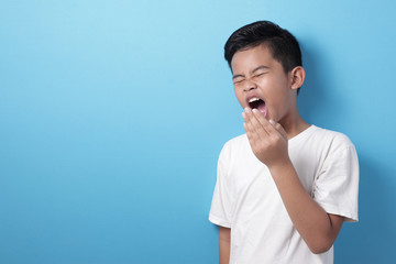 Tired Asian boy slept yawning against blue background