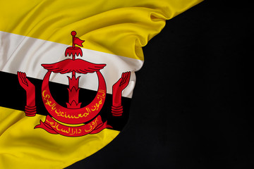 silk national flag of state of Brunei folded onto black blank form, concept of tourism, economy, politics, emigration