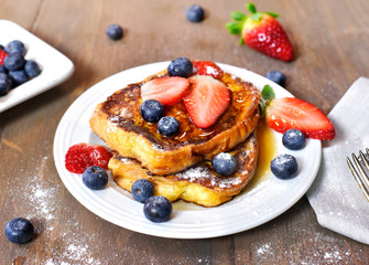 Delicious french toast with fresh fruits and maple sirup. Tasty breakfast scene or dessert with toast, strawberries, blueberries and powdered sugar. - obrazy, fototapety, plakaty