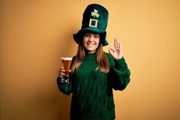 Young beautiful woman wearing green hat drinking glass of beer on saint patricks day smiling...