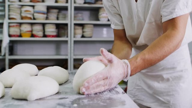 baker works with dough at metal table in workshop closeup