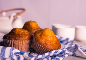  Three delicious muffins on a blue rag. Accompanied by a teapot and three cups. Light background. Horizontal format