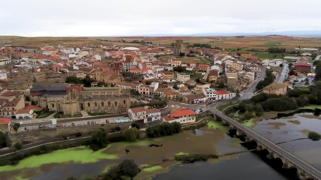 Beautiful aerial panoramic view of historic city Alba de Tormes, Castilla y Leon region, Spain. Ancient city on riverfront in a cloudy day. Drone pan from right to left