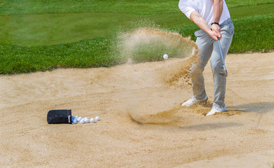 Golf coach hitting ball on sand trap.