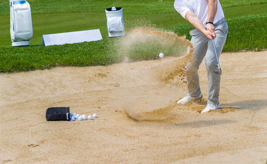 Golf coach hitting ball on sand trap.
