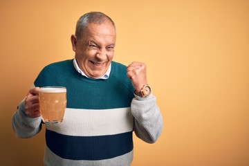 Senior handsome man drinking jar of beer standing over isolated yellow background very happy and...