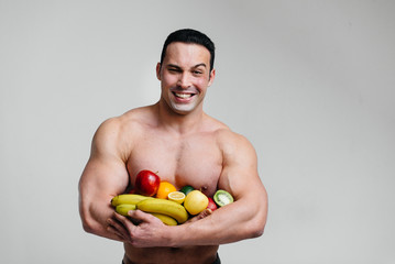 Sporty sexy guy posing on a white background with bright fruits. Diet. Healthy diet