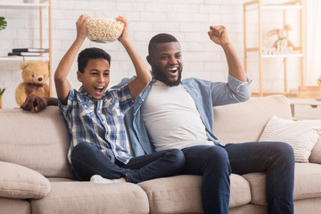 Excited Black Father And Son Watching Sports On Television And Cheering