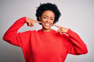 Fototapeta na wymiar Young beautiful African American afro woman with curly hair wearing red casual sweater smiling cheerful showing and pointing with fingers teeth and mouth. Dental health concept.