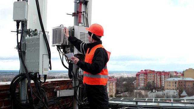 technical worker male in the bright protective clothing works on the roof near the antenna and takes notes in a notebook