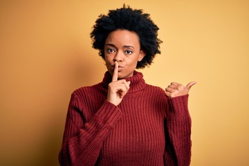 Young beautiful African American afro woman with curly hair wearing casual turtleneck sweater asking to be quiet with finger on lips pointing with hand to the side. Silence and secret concept.