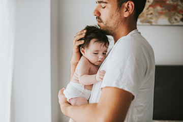 father with eyes closed hugging his baby - obrazy, fototapety, plakaty