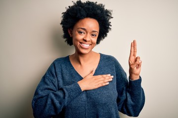Young beautiful African American afro woman with curly hair wearing casual sweater smiling swearing with hand on chest and fingers up, making a loyalty promise oath