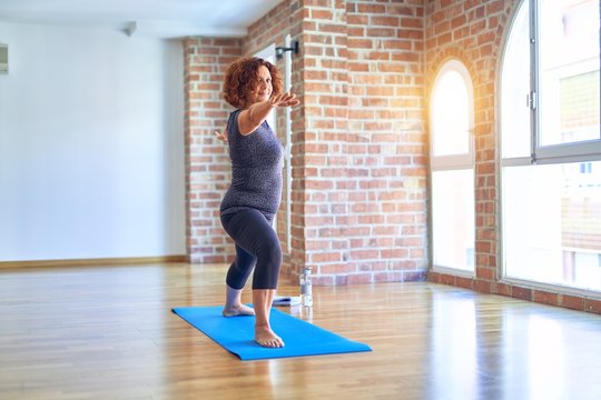 Middle age beautiful sportwoman smiling happy. Standing on mat practicing yoga doing warrior pose at gym