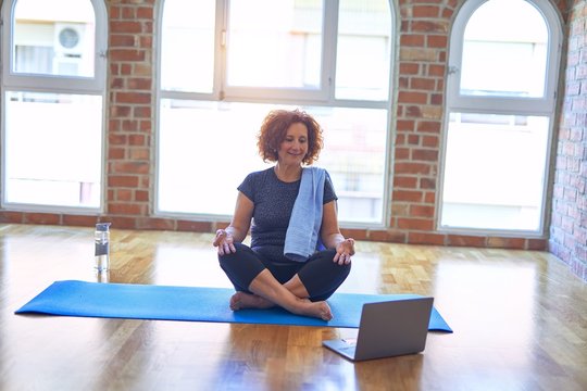 Middle age beautiful sportswoman smilig happy. Sitting on mat with smile on face using laptop at home