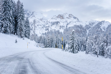 Snowy alpine road at the foot of towering mountains on a cloudy winter day