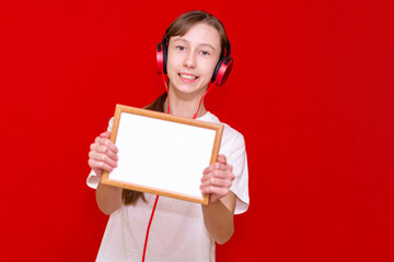 Front view portrait of a caucasian girl  listening to music and showing blank paper in a frames.Mock up,banner,copy space.Bright red studio isolated background.