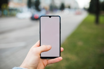 Mockup of male hand holding smartphone with blank display and finger on screen in the city