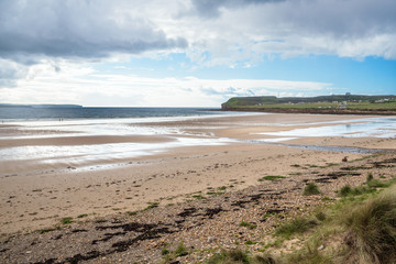 Majestic sandy beach along the north coast of Scotland on a partly cloudy spring day. Two people with a dog walking along the shore are visible in distance.