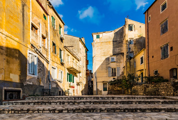 Fototapeta na wymiar Typical street of old town Corfu city Kerkyra, Greece. Sunny summer day, yellow houses, no people because of Siesta time.