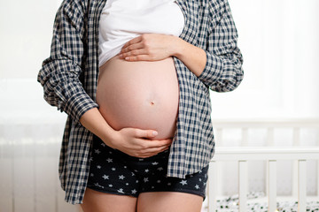 A young pregnant woman shows off her naked tummy. White window in the background. Concept of pregnancy and motherhood