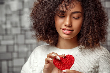 close-up portrait of a young curly-haired African American girl in a white sweater holding a paper...
