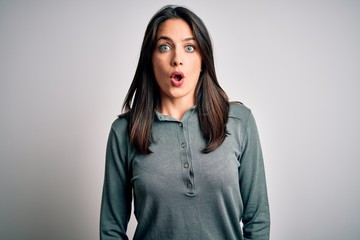 Young brunette woman with blue eyes wearing casual green sweater over white background afraid and shocked with surprise expression, fear and excited face.