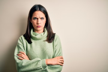 Young brunette woman with blue eyes wearing turtleneck sweater over white background skeptic and nervous, disapproving expression on face with crossed arms. Negative person.