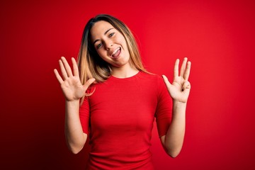 Young beautiful blonde woman with blue eyes wearing casual t-shirt over red background showing and...
