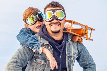 Dad and son wearing pilot glasses imitate pilots, holding a wooden plane in their hands